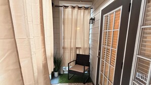 Ein schmaler Flur mit Teppichmuster, einem Sessel, einer Zimmerpflanze und einem Fenster mit Jalousien.