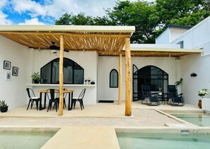 Ein überdachter Außenbereich mit Pool, ausgestattet mit Tisch und Stühlen und einer Pergola.
