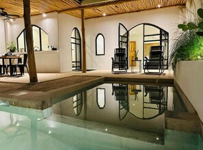 Ein moderner Poolbereich im Innenbereich mit großen Glaswänden, schwarzen Liegestühlen und einer Holzbalkendecke.