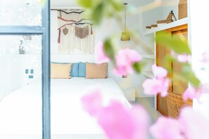 Ein modernes Schlafzimmer mit Bett, Kissen, Wandbehagung aus Makramee und einer Pendelleuchte.