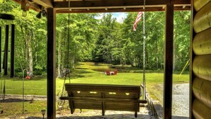 A wooden swing set with a bench in the foreground, surrounded by a lush green forest.