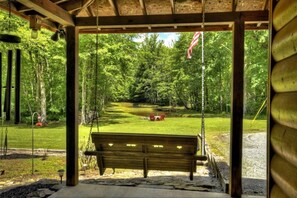 Une balançoire en bois avec un banc au premier plan, entourée d’une forêt verdoyante et luxuriante.