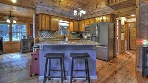 A spacious kitchen with wooden cabinets, granite countertops, and a central island with bar stools.