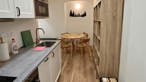 Een praktische keuken met witte kastjes, een magnetron, een spoelbak en een houten eettafel met stoelen.