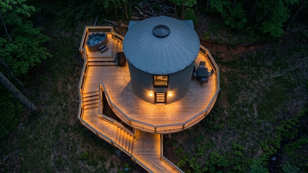 Una terrazza circolare in legno con vasca idromassaggio, area salotto e struttura coperta.