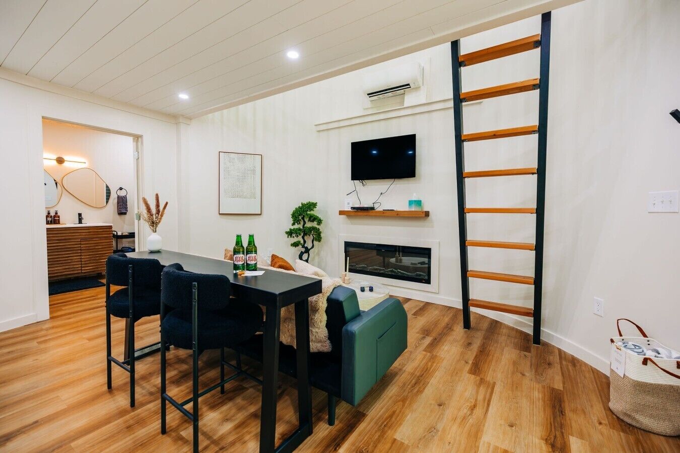 A modern living room with a dining area, a fireplace, a TV, and a wooden ladder.