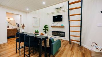 A modern living room with a dining area, a fireplace, a TV, and a wooden ladder.