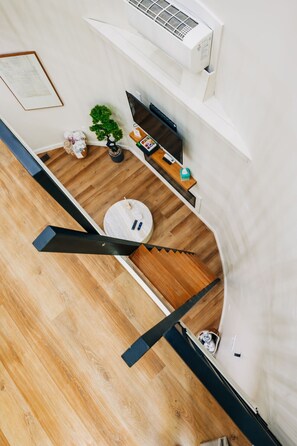 Un interior moderno con suelo de madera, una escalera, un televisor de pantalla plana, una planta en maceta y una pequeña mesa con objetos encima.