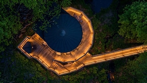 Vue aérienne d’un bâtiment circulaire doté d’un espace central ouvert, entouré d’une terrasse en bois aménagée avec des sièges.