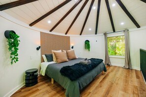 A bedroom with a bed, wooden beams, a window, and a potted plant. - NEW Romantic Silo Cabin | Outdoor Shower | Hot Tub (Beattyville)