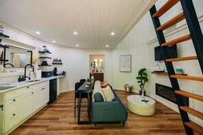 Un espacio habitable compacto con kitchenette, comedor, sofá y una escalera que lleva a un nivel superior.