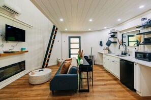 A modern kitchen with white cabinets, a black microwave, and a wooden floor. - NEW Romantic Silo Cabin | Outdoor Shower | Hot Tub (Beattyville)