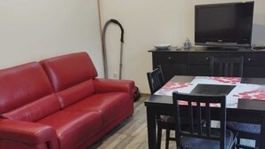 Ein rotes Ledersofa, ein Esstisch mit Stühlen, ein Fernseher und ein Staubsauger.