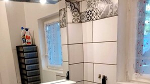 Ein Badezimmer mit einem weißen Waschbecken, einem Spiegel und einem Fenster mit floralem Vorhang.