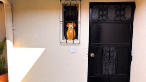 A black door with decorative metalwork, a small window with a decorative owl, and a white wall with a red trim. - Casa Luna | Best Location | Walk Everywhere (Antigua Guatemala)