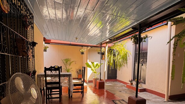 A spacious indoor area with a high ceiling, a dining table with chairs, a fan, and potted plants. - Casa Luna | Best Location | Walk Everywhere (Antigua Guatemala)