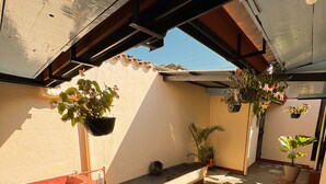 A covered outdoor area with a concrete floor, potted plants, and a red container. - Casa Luna | Best Location | Walk Everywhere (Antigua Guatemala)