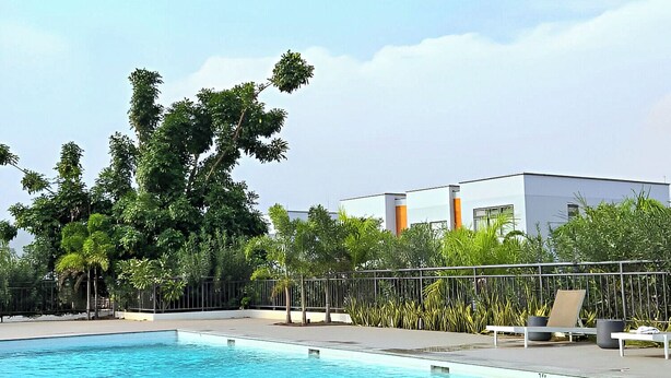 Ein Schwimmbecken mit klarem, blauem Wasser, umgeben von einem Zaun, Bäumen und einem modernen Gebäude im Hintergrund.