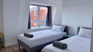 Une chambre avec deux lits, une fenêtre avec des rideaux, une petite plante et une table de chevet.