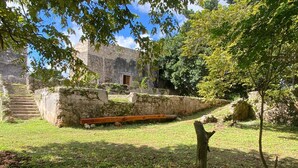 Um edifício de pedra com uma escadaria que leva a uma porta, rodeado por grama e árvores.