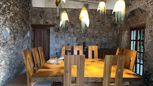 Uma área de refeições rústica com parede de pedra, mesa e cadeiras de madeira e luminárias pendentes.