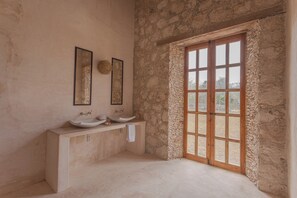 Une salle de bain avec deux lavabos, une baignoire et une grande fenêtre donnant sur un mur en pierre.