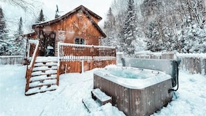 Una cabaña de madera con jacuzzi en un paisaje nevado.