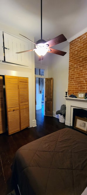 A bedroom with a bed, a ceiling fan, a brick wall, and a fireplace. - Lower Garden District Charmer with private balcony! (New Orleans)