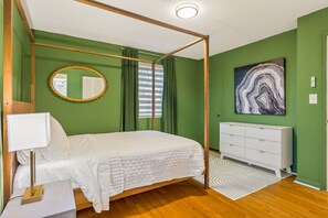 A bedroom with a four-poster bed, a white dresser, a round mirror, and a marble artwork on the wall. - The Sweet Pea of Liberty (Liberty)