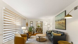 A modern living room with a sofa, armchair, coffee table, and a dining area in the background.