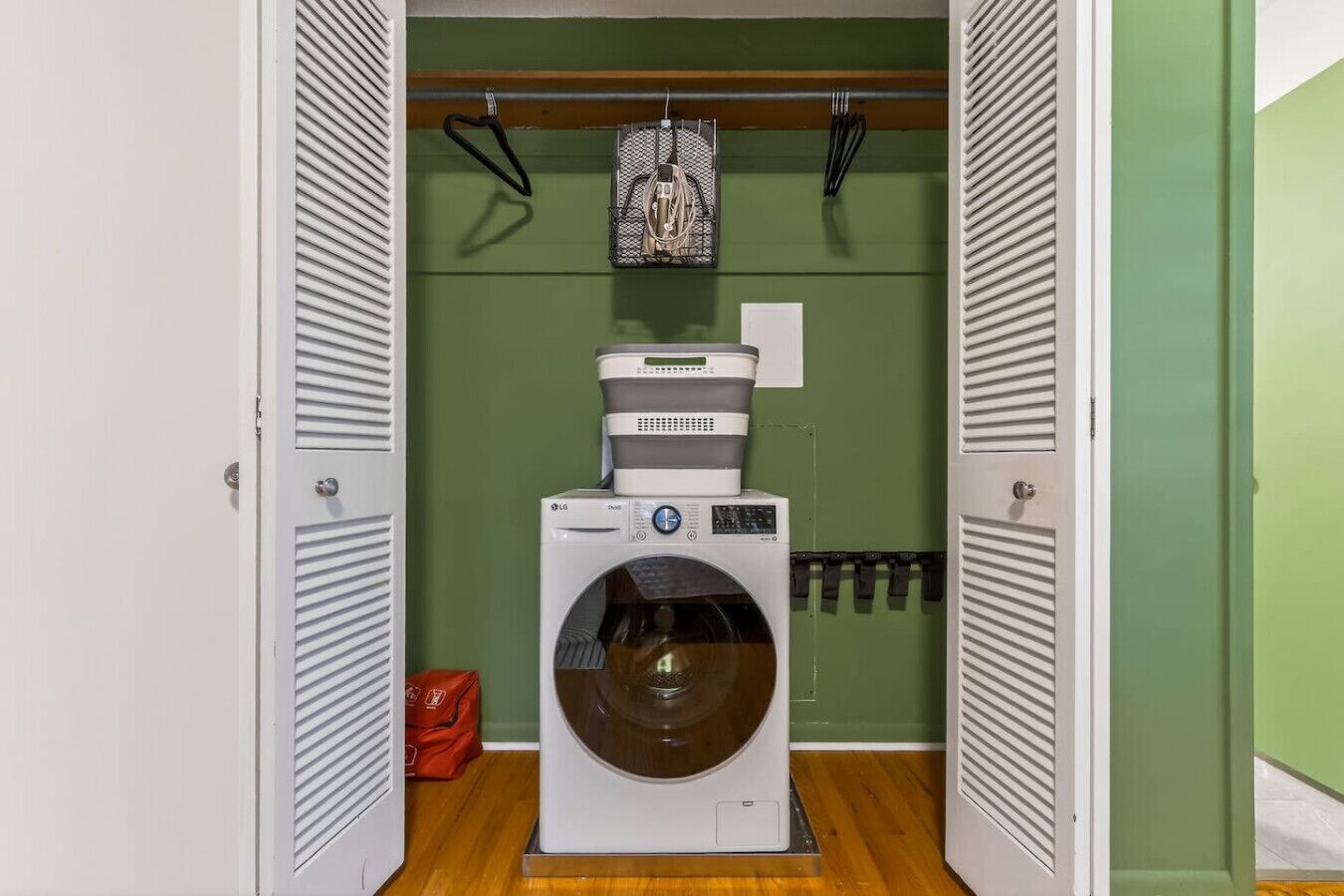 A compact laundry room with a front-loading washing machine, a drying rack, and a basket.