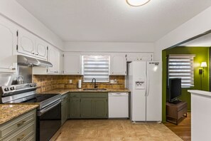A compact kitchen with white cabinets, a stainless steel stove, a dishwasher, and a refrigerator. - The Sweet Pea of Liberty (Liberty)