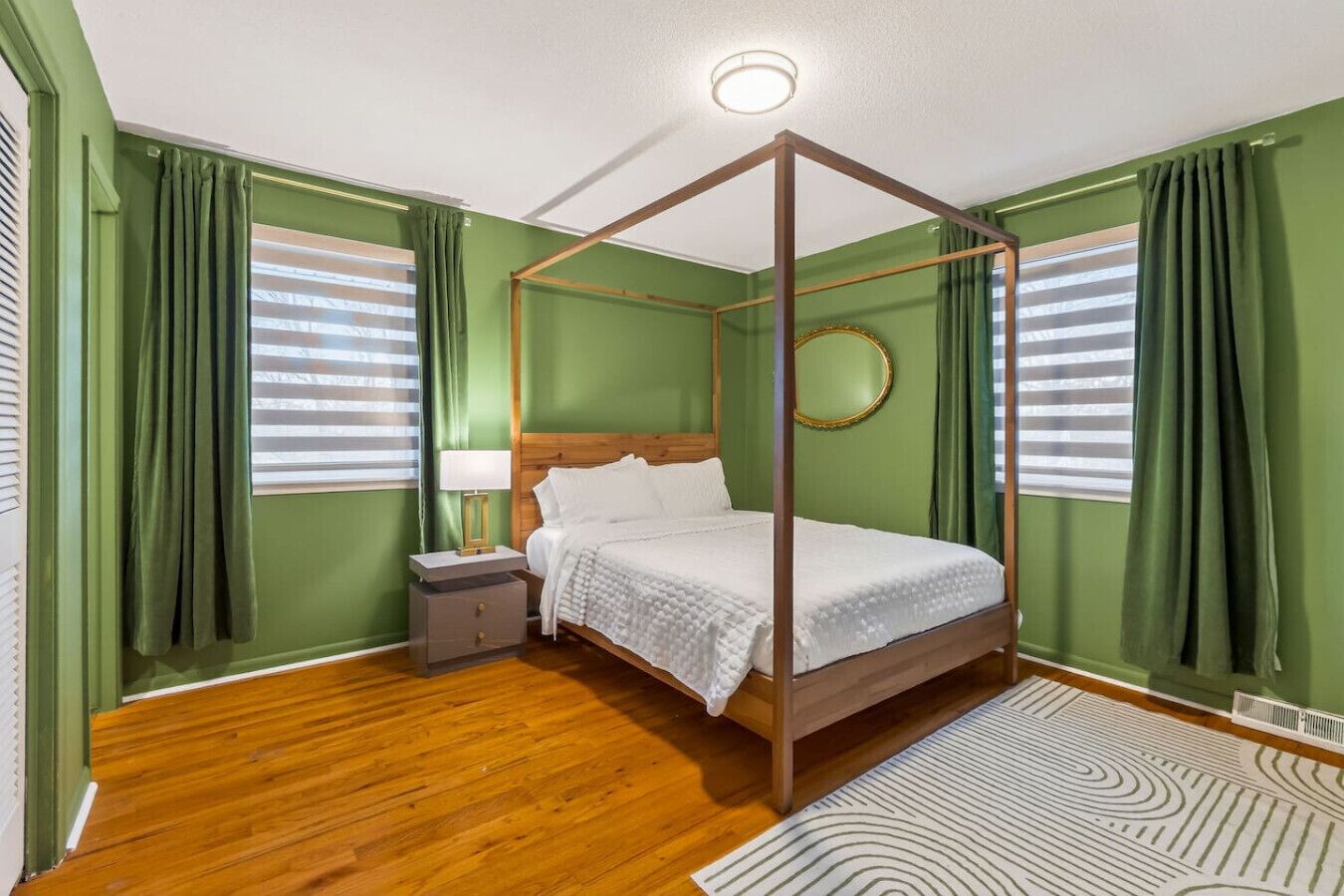 A four-poster bed in a room with green walls, wooden flooring, and a round mirror on the wall.