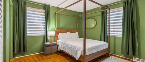 A four-poster bed in a room with green walls, wooden flooring, and a round mirror on the wall.