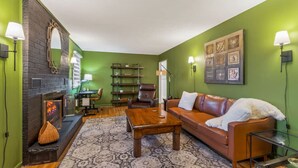 A living room with a fireplace, green walls, a leather sofa, a coffee table, and a bookshelf.