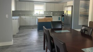 A modern kitchen with white cabinets, a wooden island, and a dining area with a dark wooden table and chairs. - Perfect 3-bedroom mobile home with AC in charming Albion. Mobility-accessible. (Albion)