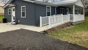 A single-story house with a dark gray exterior, white trim, and a front porch with a white railing. - Perfect 3-bedroom mobile home with AC in charming Albion. Mobility-accessible. (Albion)