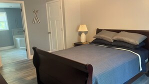 A bedroom with a bed, nightstand, lamp, and a door leading to a bathroom. - Perfect 3-bedroom mobile home with AC in charming Albion. Mobility-accessible. (Albion)