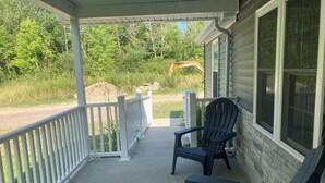 A covered porch with a white railing, a black Adirondack chair, and a view of a construction site in the background. - Perfect 3-bedroom mobile home with AC in charming Albion. Mobility-accessible. (Albion)