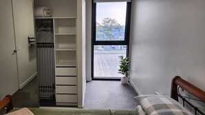 Kapea käytävä, jonka oikealla puolella on sänky, patteri ja ikkuna, josta avautuu näkymä kadulle ja rakennuksiin.