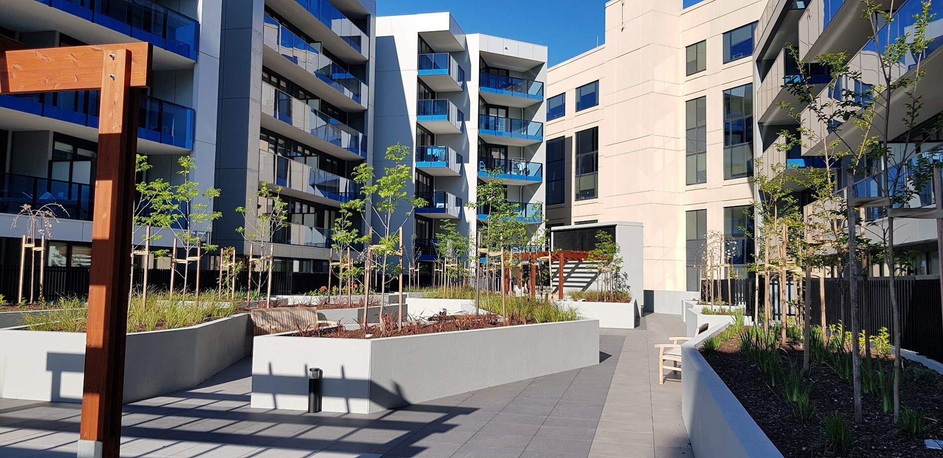 Ein moderner Wohnkomplex in der Stadt mit mehreren Wohngebäuden, gemeinsamen Außenbereichen und viel Grün.