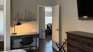 Un dormitorio con cama, escritorio, silla, cómoda y televisor montado en la pared.