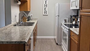 Una cocina con armarios de madera, encimera de granito, microondas, refrigerador y estufa de acero inoxidable.