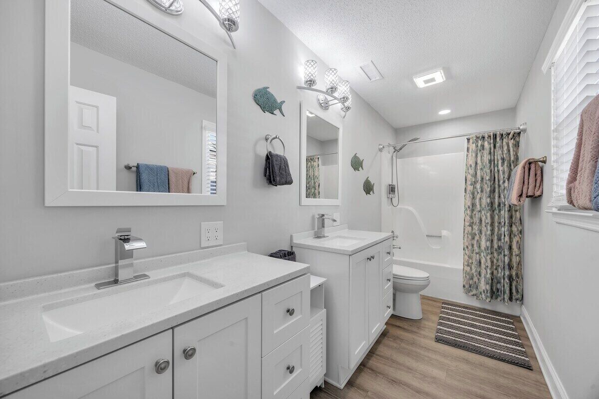 A modern bathroom with a large mirror, two sinks, a toilet, and a shower.
