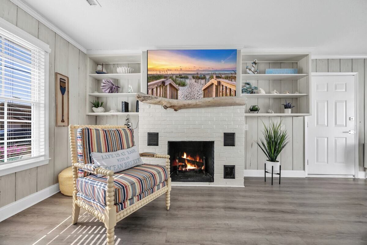 A living room with a fireplace, a striped armchair, and a large painting of a beach scene.