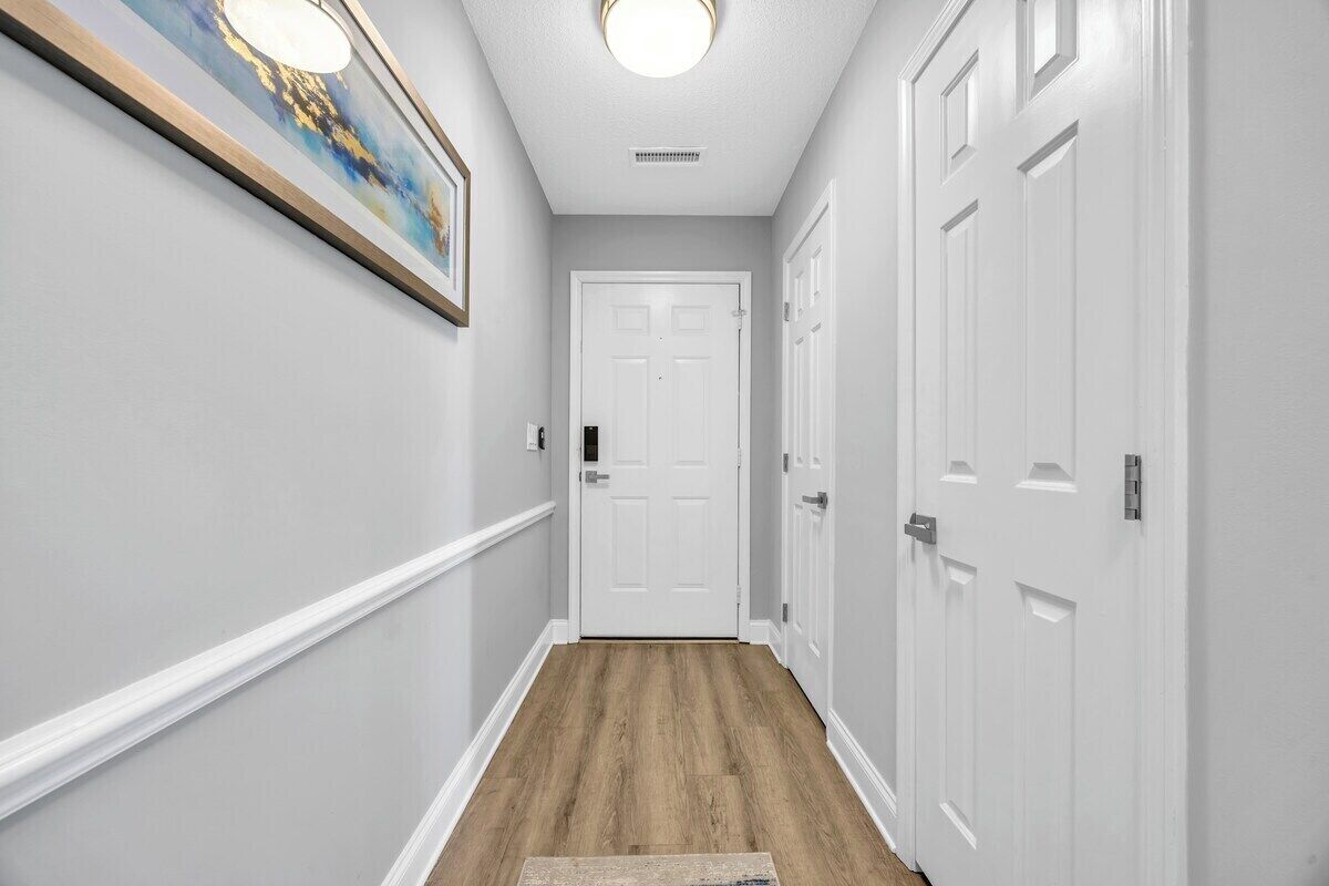 A hallway with a wooden floor, white walls, and a white door at the end.