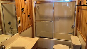 Un baño con paneles de madera, cabina de ducha de vidrio, inodoro y lavamanos con espejo.