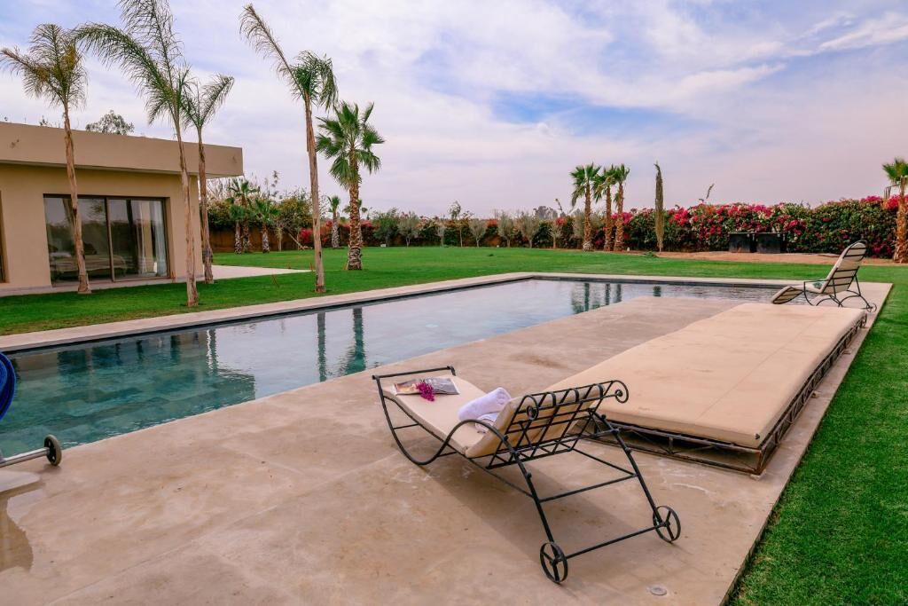 A swimming pool with lounge chairs and a sunbed, surrounded by palm trees and a well-maintained lawn.