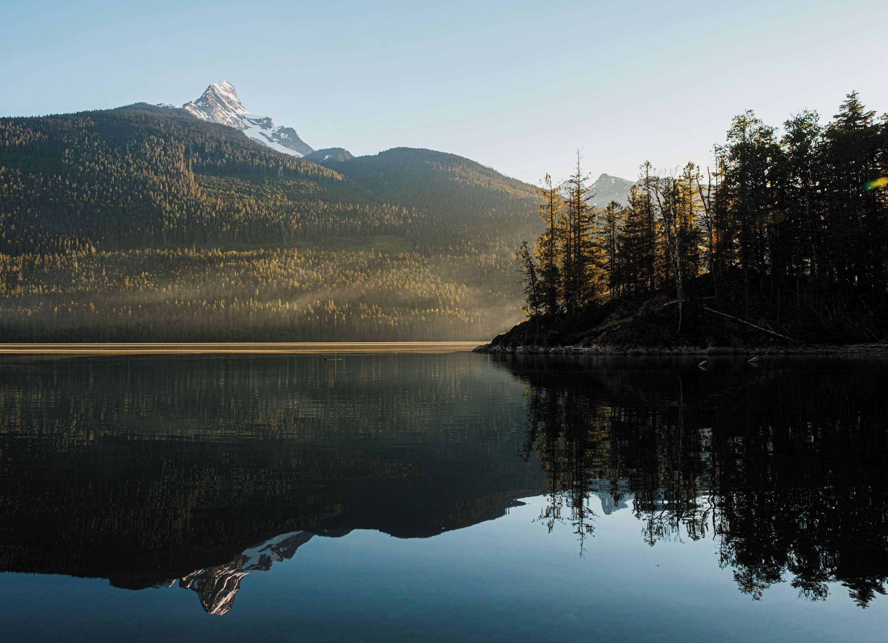 A calm lake with a mountain in the background and a forested area to the right.