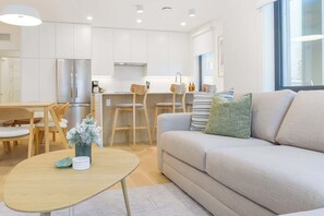 A modern living room with a sofa, a coffee table, and a dining area with chairs. - Summit Central -Bright Condo with Private Hot Tub (Revelstoke)